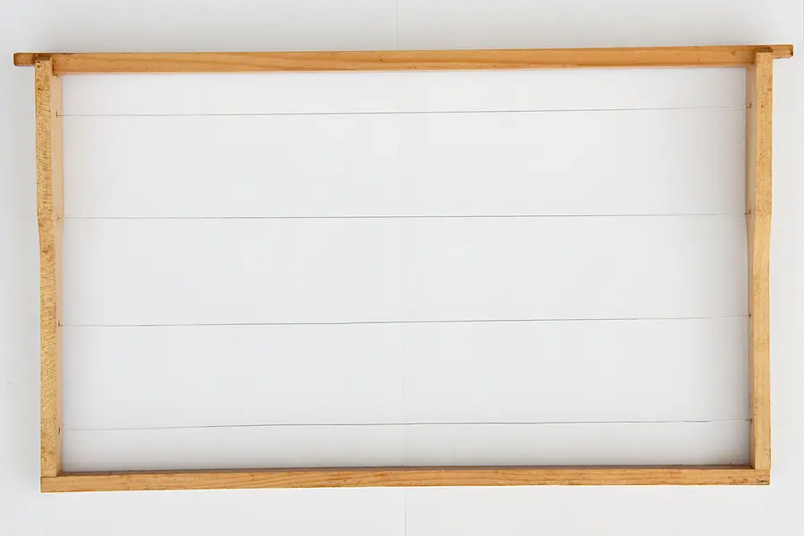 Empty wooden hive frame with horizontal wires stretched across it, ready to hold a beeswax foundation sheet