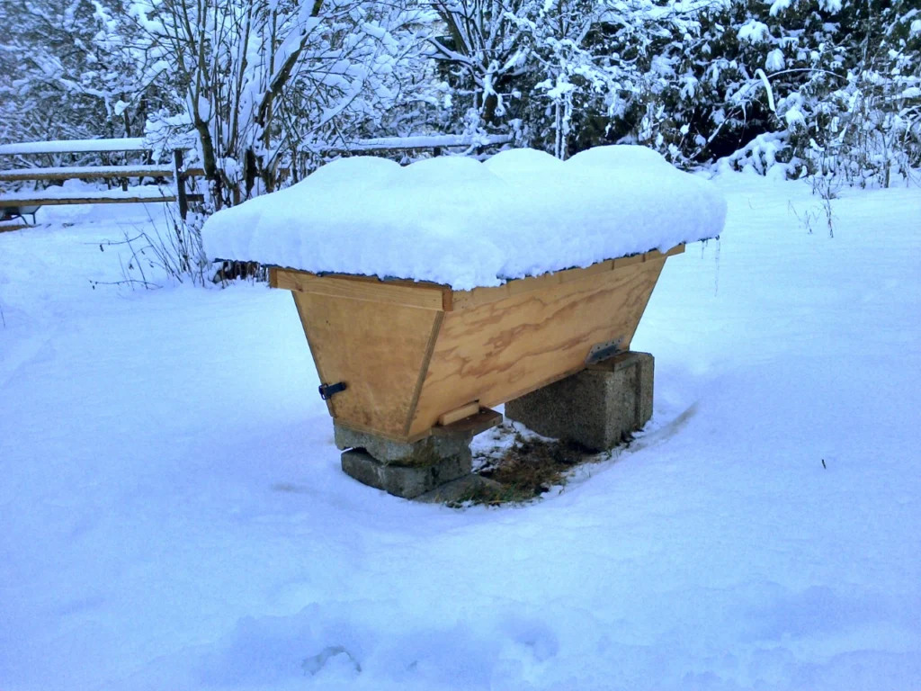 A beehive covered in snow during winter, the conditions hive insulation and moisture management are designed to address