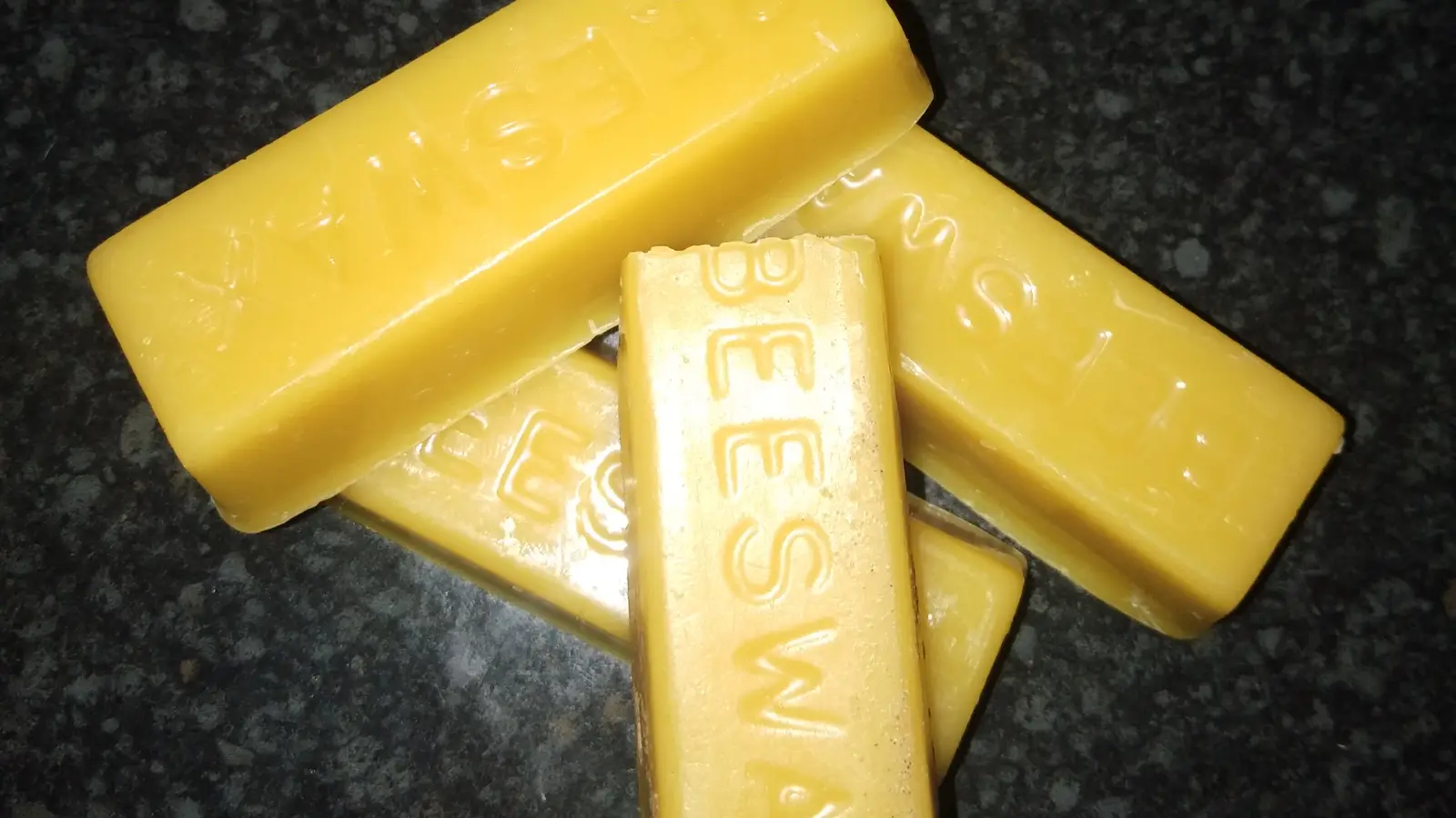 Four molded yellow beeswax bars stamped BEESWAX, the front bar dusted with a pale film