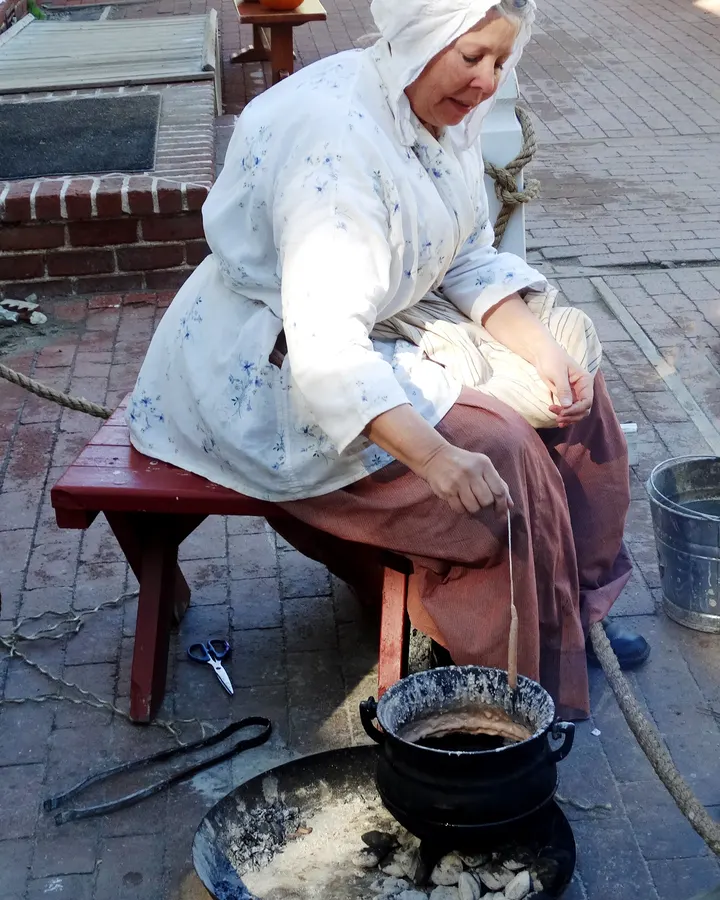 Costumed interpreter hand-dipping candles from a black kettle of melted wax at a California living history farm