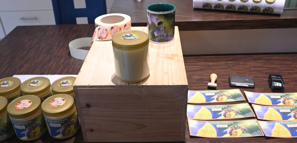 Filled honey jars with printed labels and lid stickers laid out on a bench beside a roll of blank labels