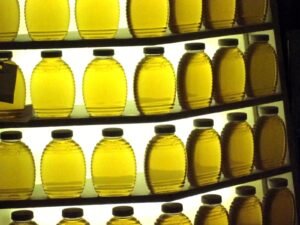 Photo of rows of clear, light amber honey jars backlit on shelves at a state fair honey display