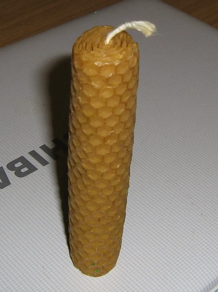 Rolled beeswax candle made from a honeycomb-patterned foundation sheet, with its cotton wick on top
