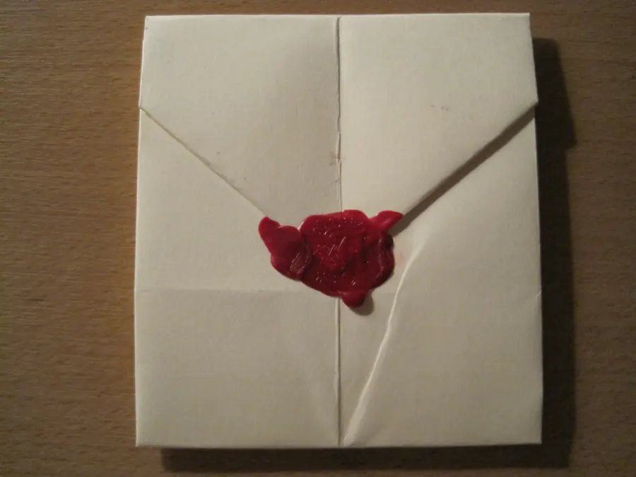 Red wax seal pressed with a letter A closing a hand-folded paper letter on a wooden table