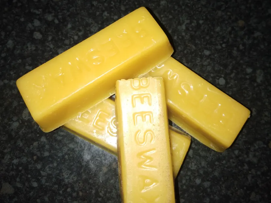 Four small bars of natural yellow beeswax stamped with the word beeswax on a dark countertop