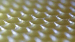 Close-up macro of embossed beeswax foundation showing rows of hexagonal cell bases in pale yellow wax