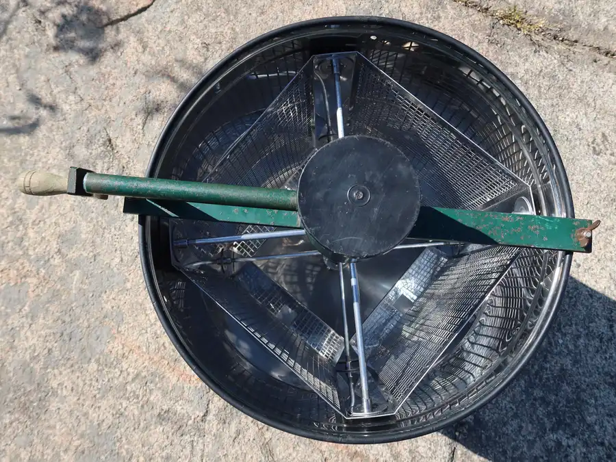 Empty manual honey extractor seen from above, showing the steel drum, frame basket and center shaft