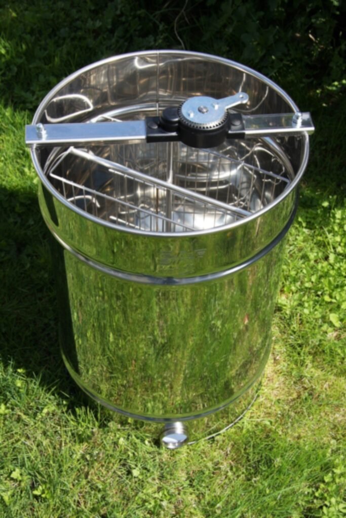 Photo of an empty stainless steel four-frame honey extractor with a hand crank, a food-safe metal for honey contact