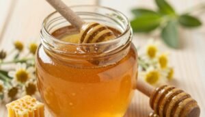 A close-up view of raw honey in a glass jar, showcasing its thick, amber-golden texture with tiny bubbles and natural