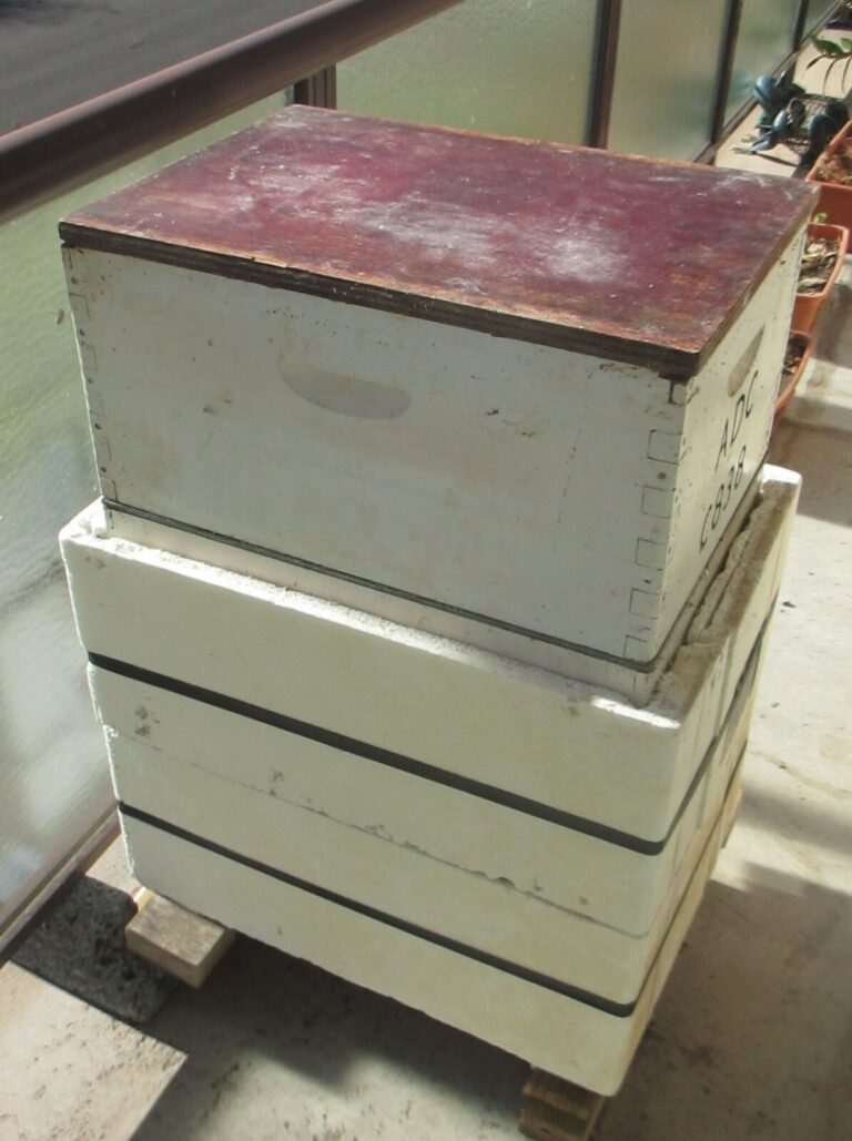 Photo of a Langstroth hive whose lower boxes are wrapped in thick white foam board insulation, one panel per box, with an unwrapped top box
