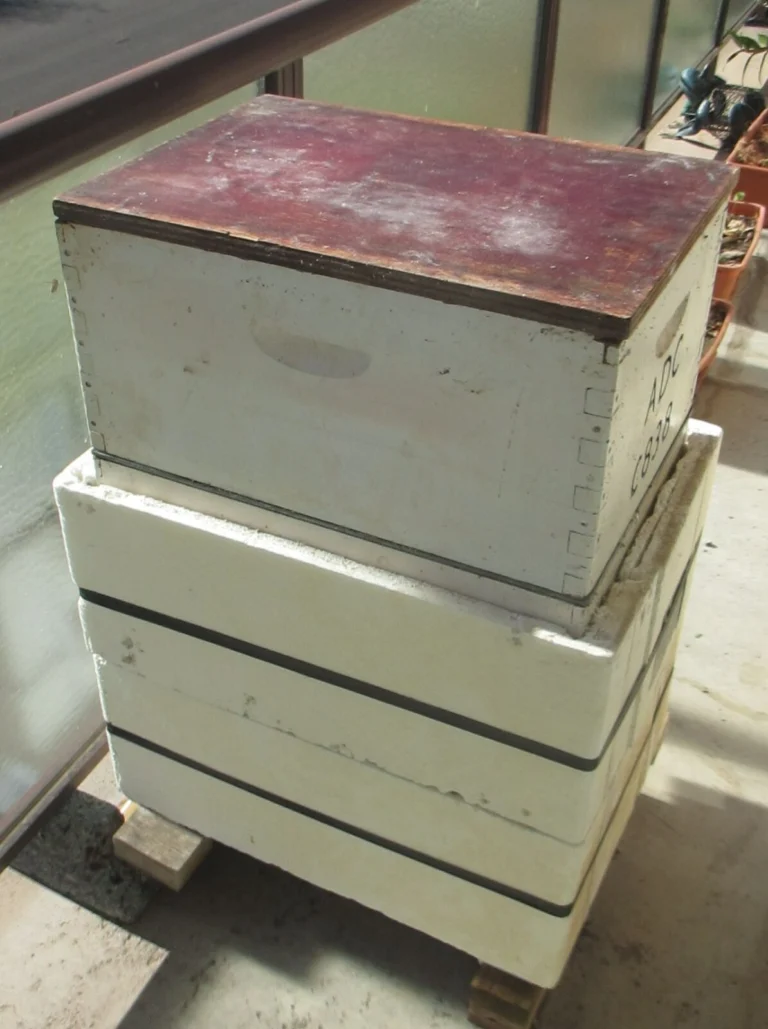 Photo of a Langstroth hive whose lower boxes are wrapped in thick white foam board insulation, one panel per box, with an unwrapped top box