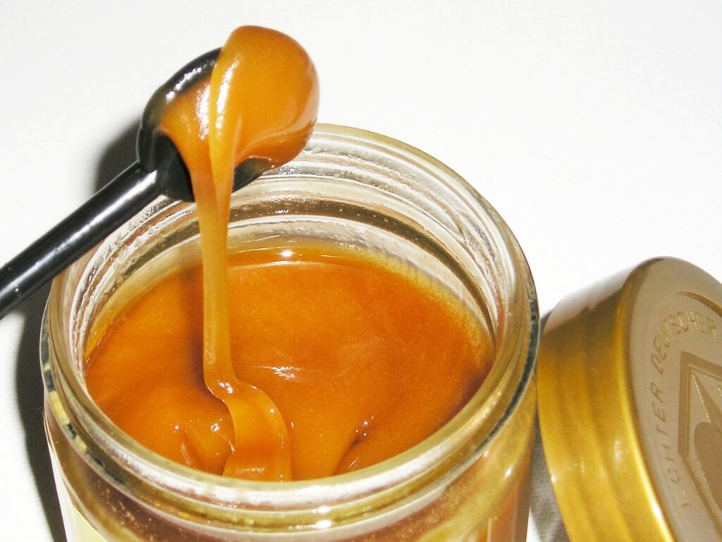 Photo of thick dark amber buckwheat honey dripping from a spoon into an open glass jar