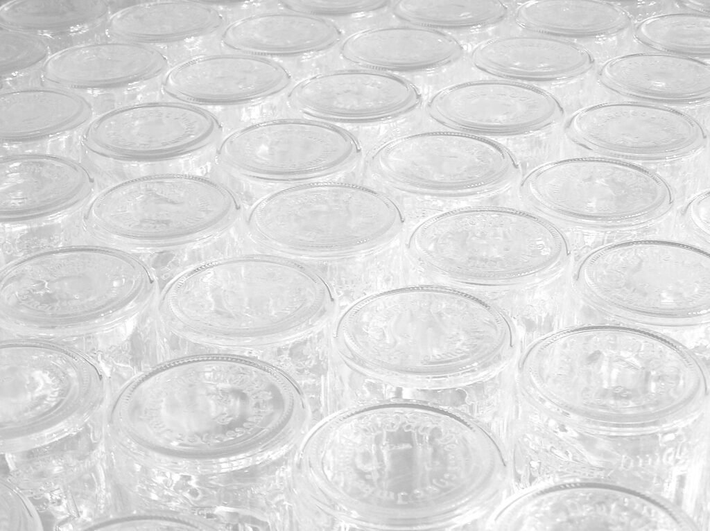 Photo of rows of empty clear glass honey jars ready to be filled after the honey harvest