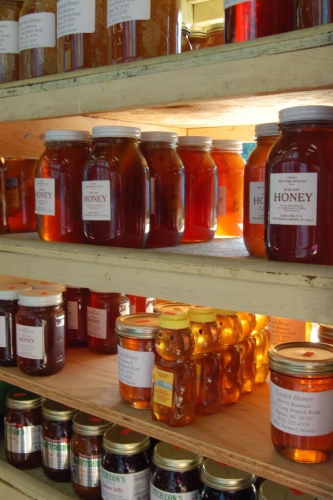 Photo of shelves of labeled jars of local honey in several colors and sizes for sale at a farmers market