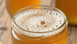 Close-up photo of a jar of amber honey with a layer of fine white foam bubbles on the surface after bottling
