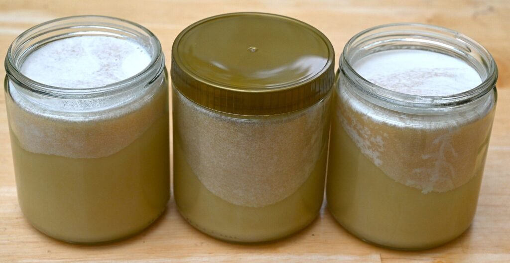 Photo of three jars of pale crystallized honey with white frosting blooms on the surface and the upper glass