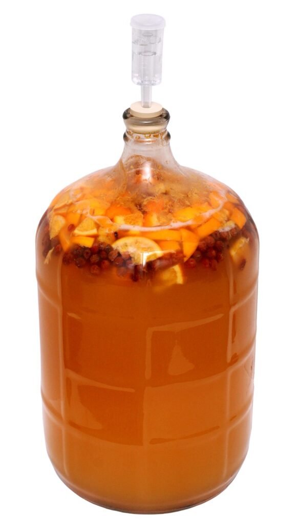 Photo of homemade honey and fruit mead fermenting in a glass carboy sealed with a plastic airlock