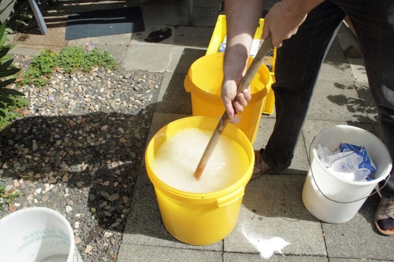 Photo of a beekeeper stirring sugar and water together in a yellow bucket to make syrup for feeding bees