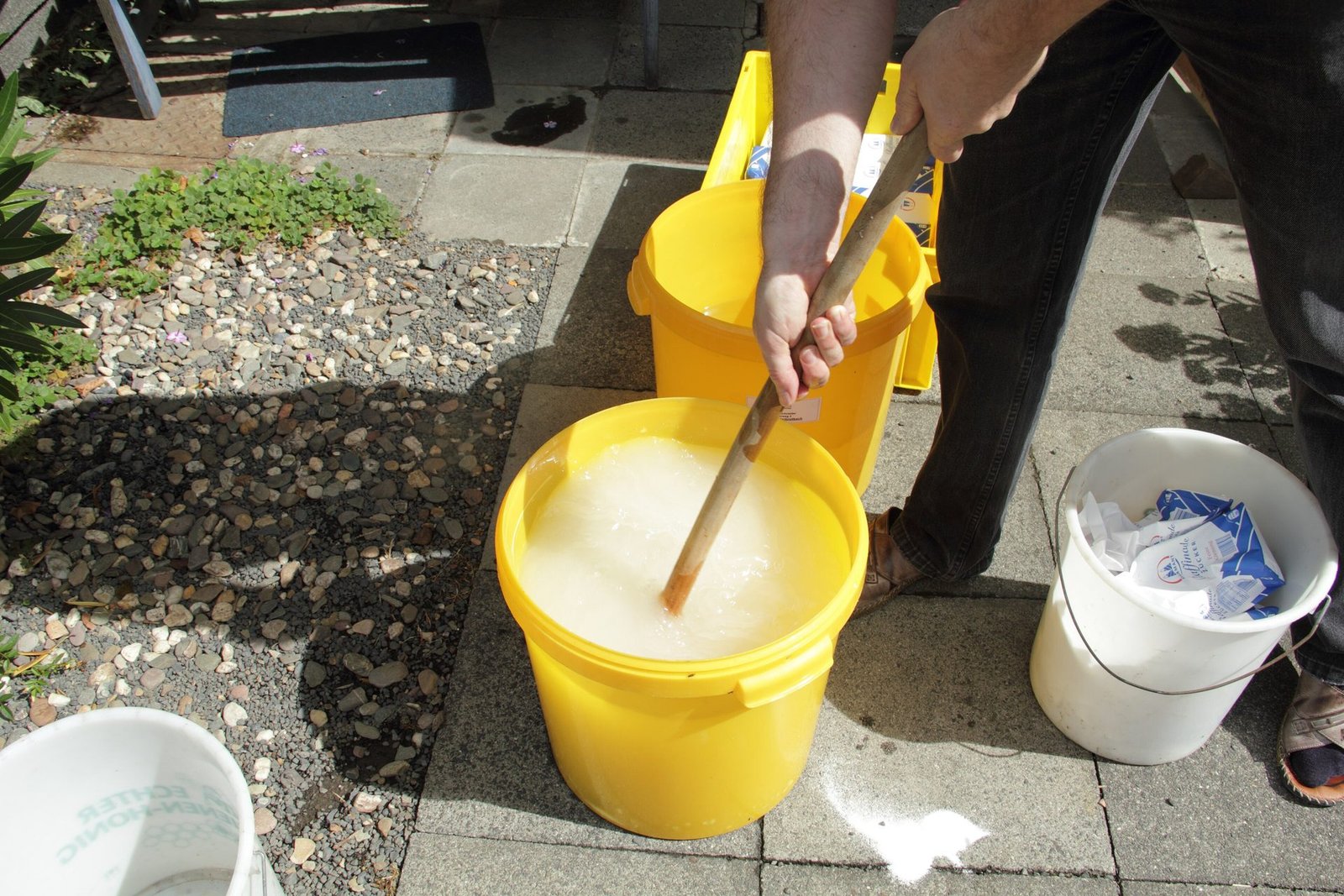 Photo of a beekeeper stirring sugar and water together in a yellow bucket to make syrup for feeding bees