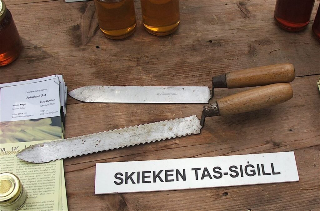 Photo of two cold uncapping knives on a wooden table, one with a straight blade and one with a serrated edge