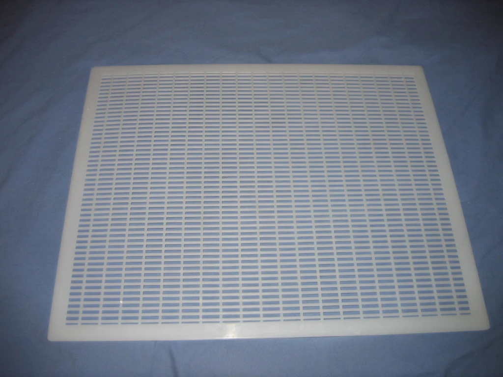 Photo of a white plastic queen excluder with slots that let workers pass but block the larger queen