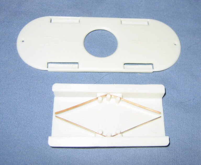 Photo of a white plastic Porter bee escape taken apart, showing its two thin bronze spring strips