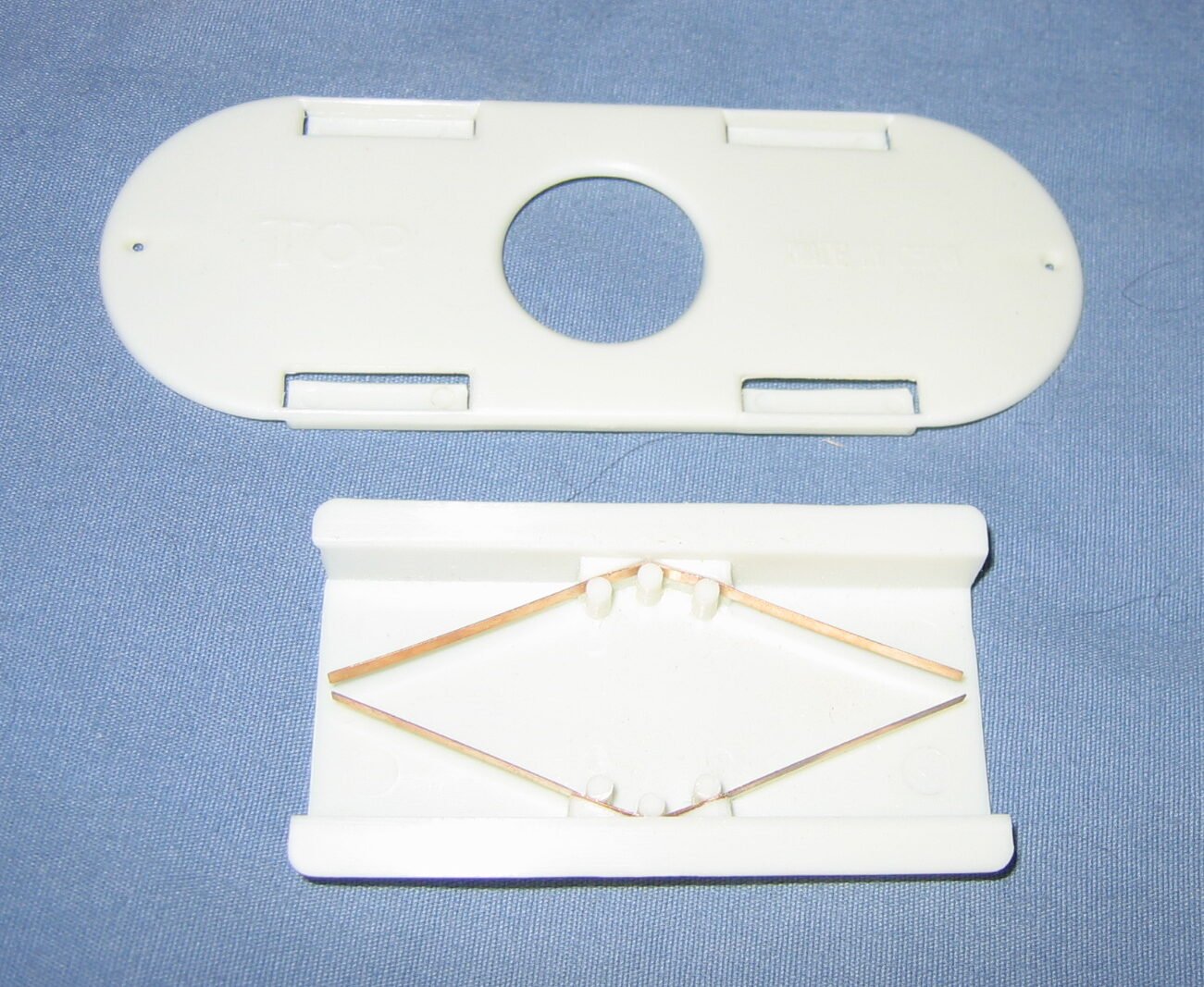 Photo of a white plastic Porter bee escape taken apart, showing its two thin bronze spring strips