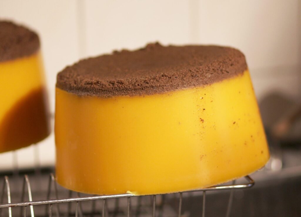 Photo of an upturned block of yellow rendered beeswax with a brown layer of settled debris on its underside