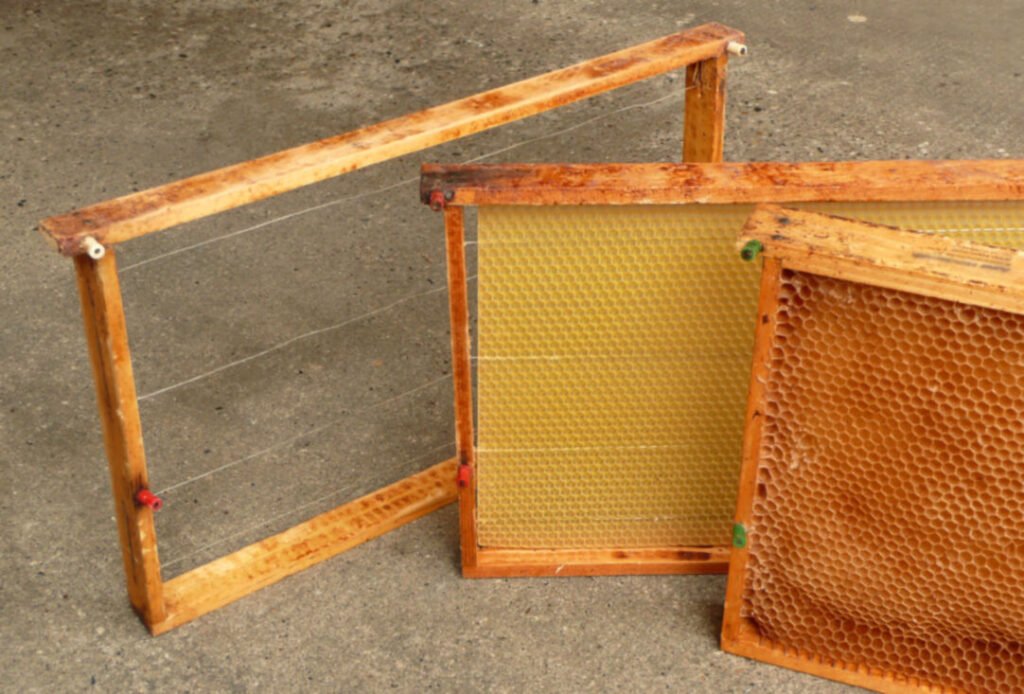 Photo of three hive frames side by side: an empty wired frame, a frame with wax foundation, and drawn comb