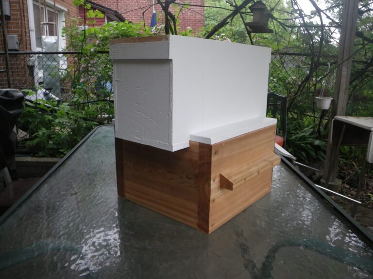 Photo of a painted wooden 5-frame Langstroth nuc box sitting on top of a cedar Warré hive box