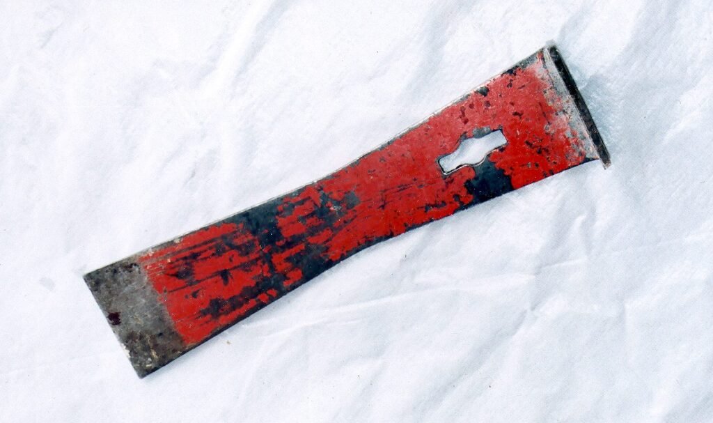 Photo of a worn red-painted steel hive tool with a flat scraper end, the kind of tool carried from yard to yard