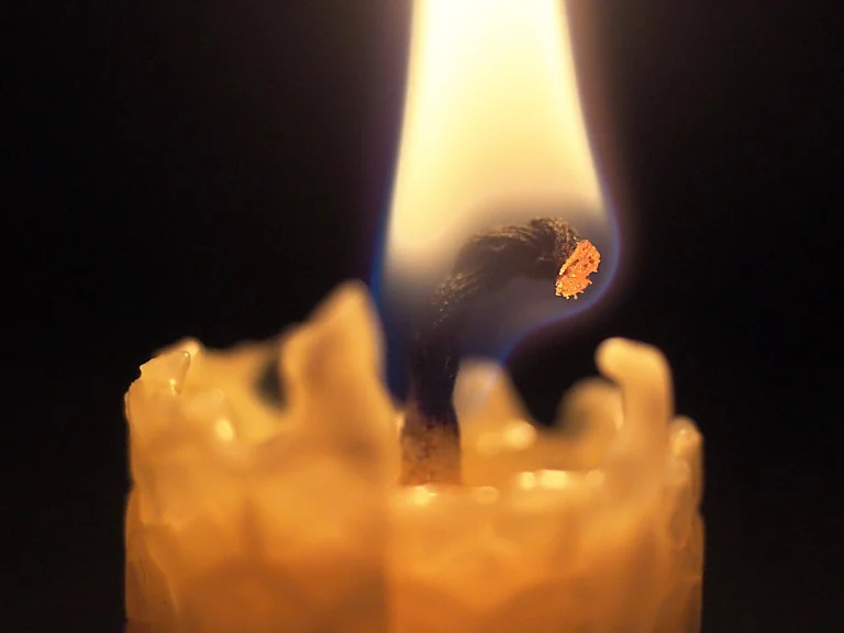Closeup of a beeswax candle burning with a glowing wick