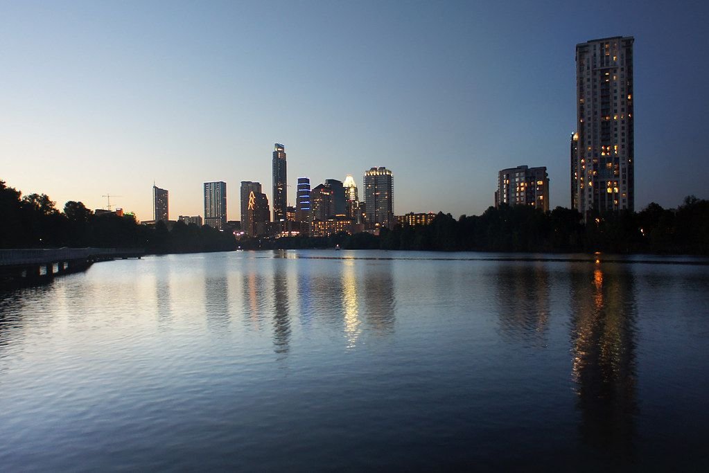 Austin, Texas skyline at dusk viewed across a lake, with downtown high-rise buildings reflected in the water