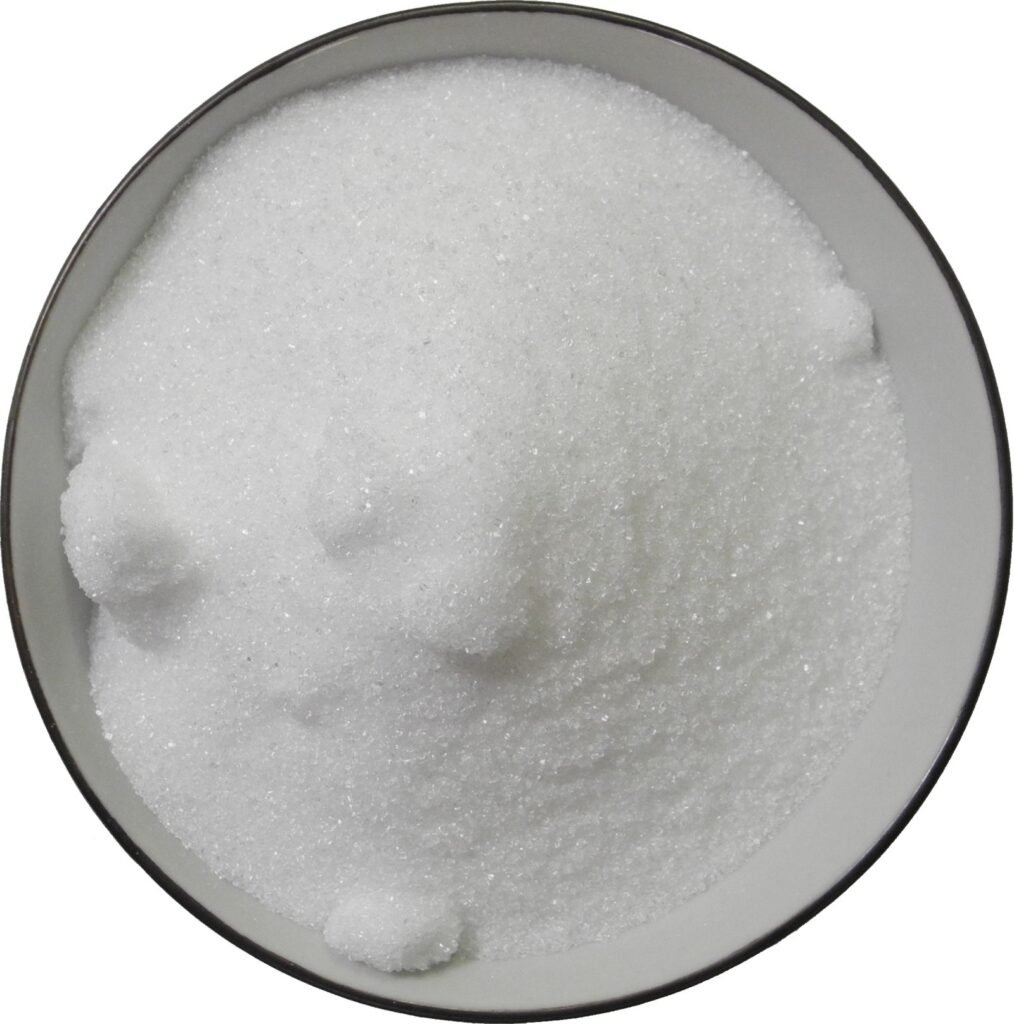Close-up of granulated white sugar crystals in a bowl, the pure sucrose structure that caramelizes and behaves differently in a recipe than honey's liquid fructose-glucose blend