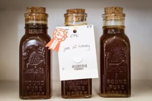 Three labeled glass jars of honey with ribbon tags on display at a local fair judging table