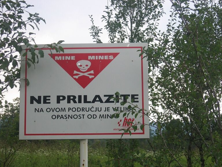 A red and white minefield warning sign reading NE PRILAZITE (Do Not Approach) with a skull and crossbones, posted in rural Croatia