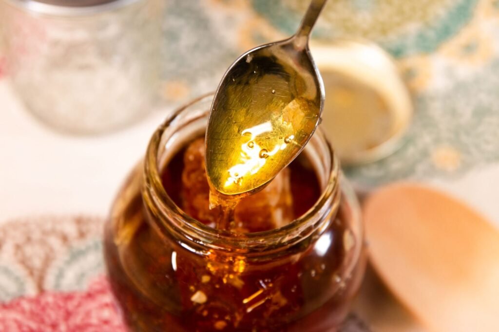 A spoon drizzling raw liquid honey into a small jar, the same honey used to fill sealed honey sticks