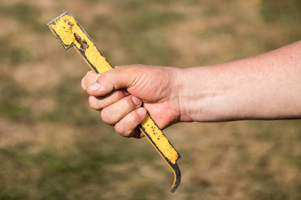 Close-up of a beekeeper's hand gripping a yellow hive tool used for research apiary inspections