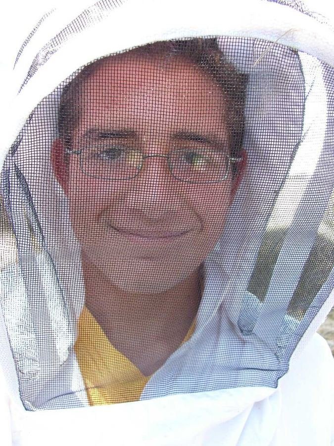 Beekeeper wearing protective veil and suit gear while inspecting a hive