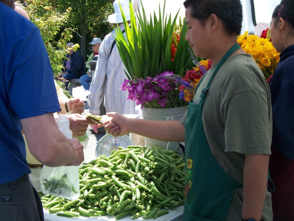 A customer completing a cash transaction with a vendor at a farmers market, the standard sales method most markets require for customer-facing sales