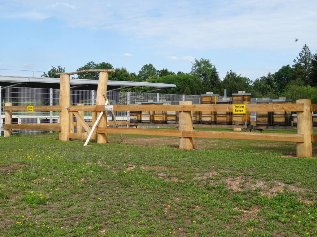 Beehives behind a fenced caution-bees sign on a corporate manufacturing campus in Germany