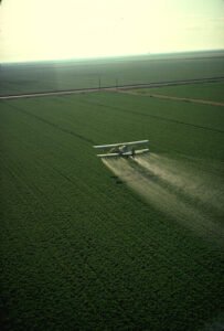 Crop duster airplane spraying pesticide over a large agricultural field