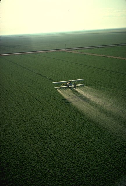 Crop duster airplane spraying pesticide over a large agricultural field