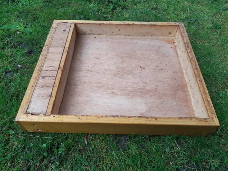 Empty wooden hive feeder box with dirt and residue buildup that needs cleaning between colonies