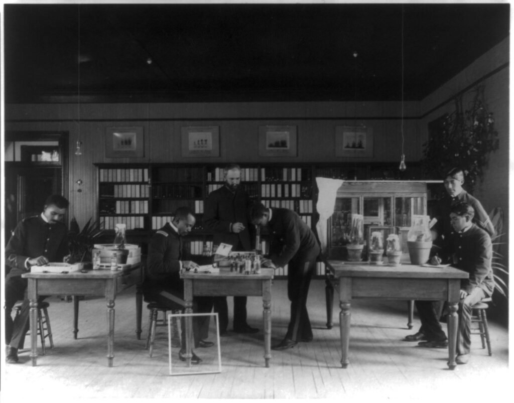 Historic photo of a teacher and students studying insects together in a laboratory classroom, the kind of educational apiary program a hive donation can support