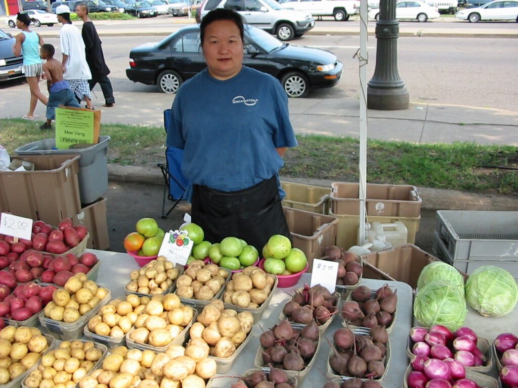A farmers market vendor tending her produce stall, the kind of neighboring vendor a beekeeper might trade honey with after the market closes