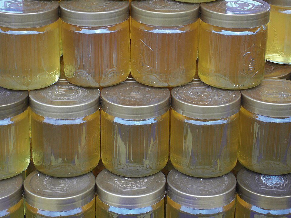 Rows of stacked glass jars filled with golden raw honey, the kind of retail product covered by honey authenticity certification programs