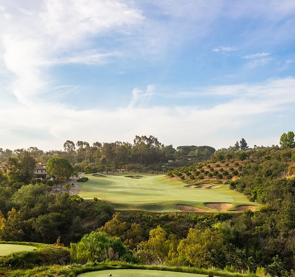 Golf course fairway framed by dense natural rough and tree-lined out-of-play areas, the kind of acreage pollinator certification programs target for habitat conversion