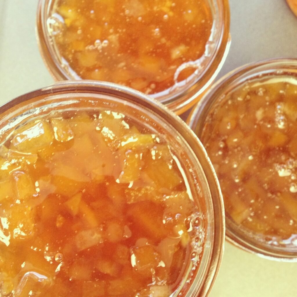 Jars of homemade citrus marmalade cooling on a counter after processing, an example of a jam where honey can replace part of the sugar