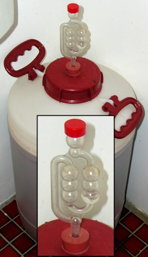 Close-up of a homebrew airlock fitted to a plastic fermentation vessel, showing how it seals the batch while venting fermentation gas